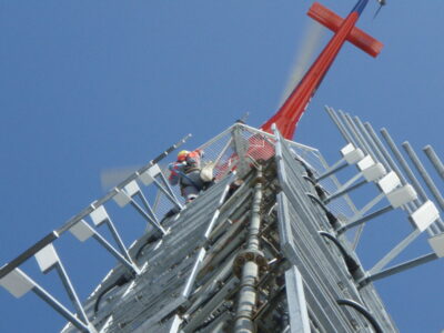 Bilde av en mast tatt nedenfra, hvor en ansatt jobber i masten.