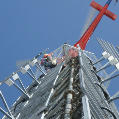Bilde av en mast tatt nedenfra, hvor en ansatt jobber i masten.