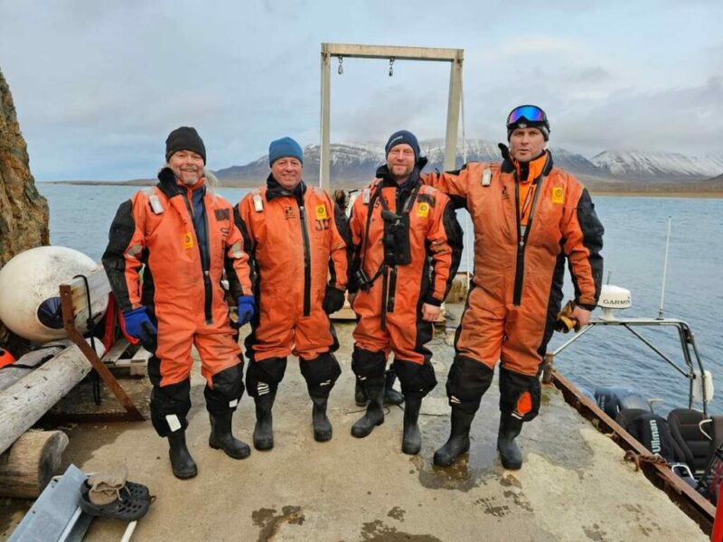 Fire ansatte står sammen på et gruppebilde på en kai, Isfjord Radio.